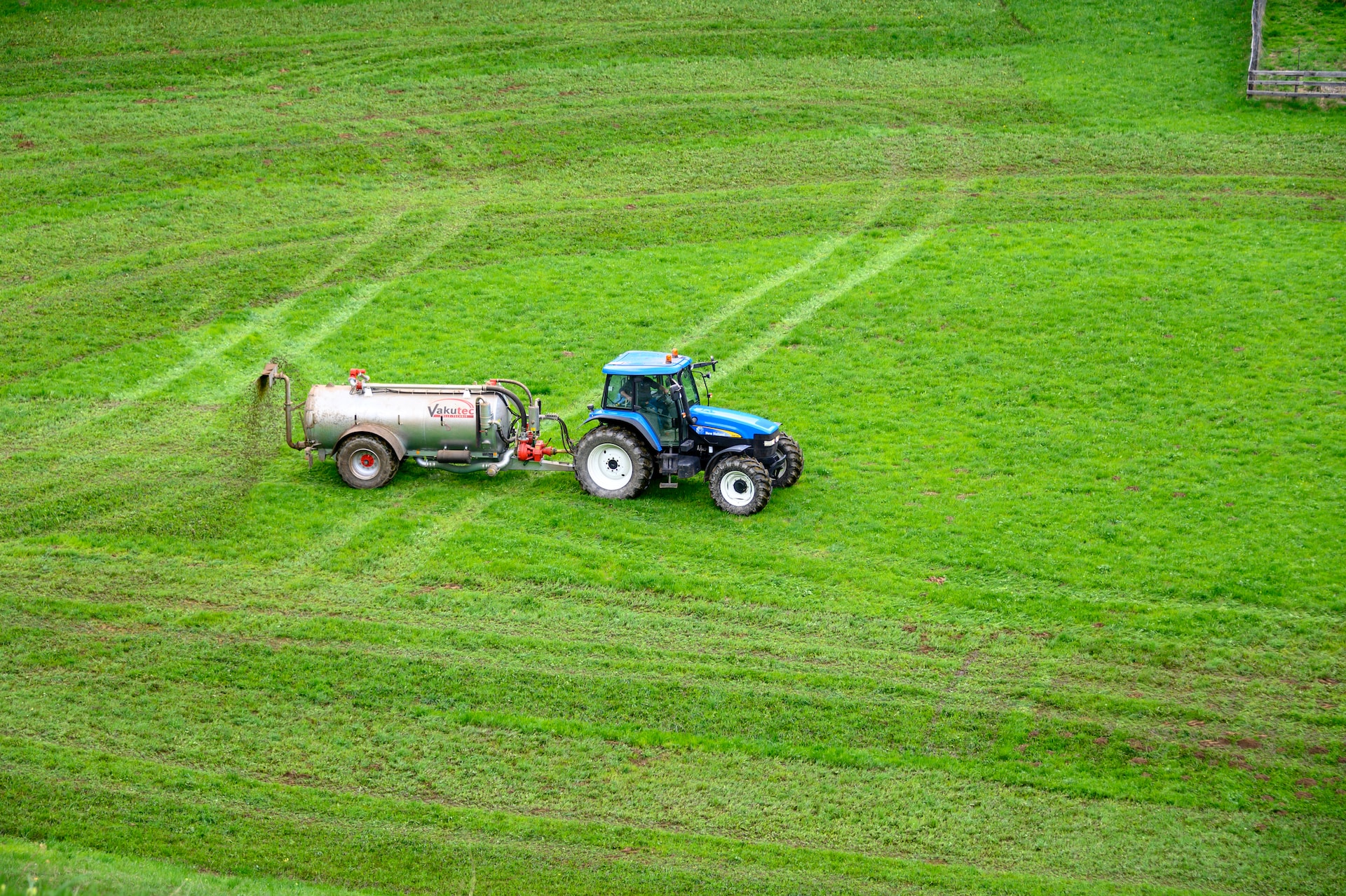 Blue tractor towing a tank spreading fertilizer on a green grass field