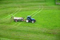 Blue tractor towing a tank spreading fertilizer on a green grass field