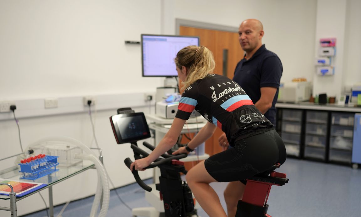 lady of exercise bike and man stood next to her