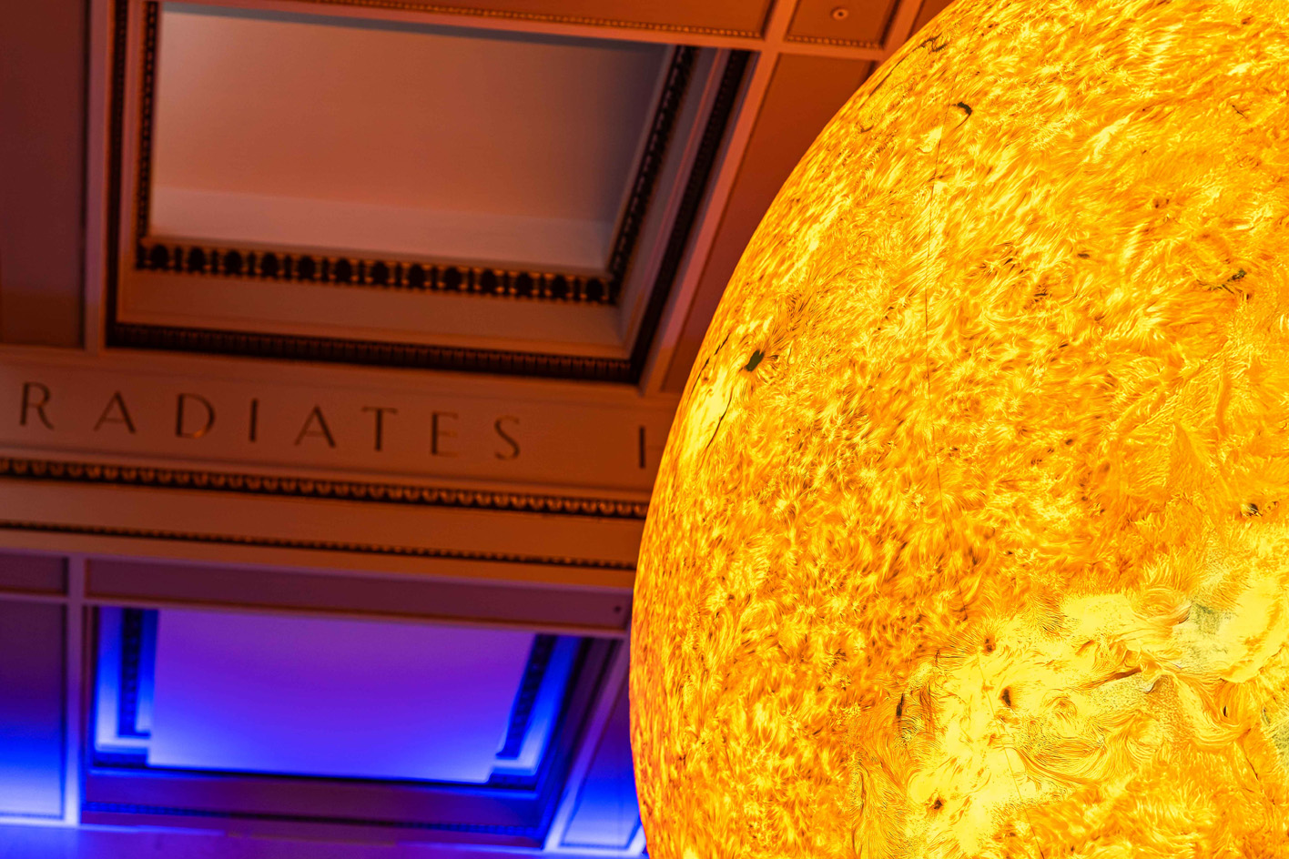 The illuminated sculpture 'Helios' by Luke Jerram with the word "radiates" in the background