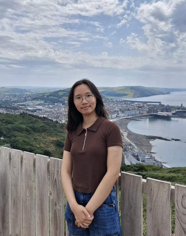 student ambassador wearing a brown top and blue jeans on fieldtrip witi city view and sea in the background