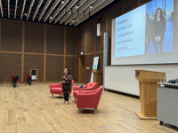 Dr. Shani Dhanda standing at the front of a lecture theatre delivering a talk