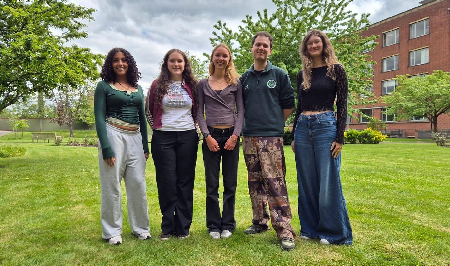 Five students standing on a lawn on campus
