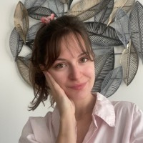 Ioulia smiles at the camera. She has brown hair in a ponytail, and is wearing a light pink shirt.