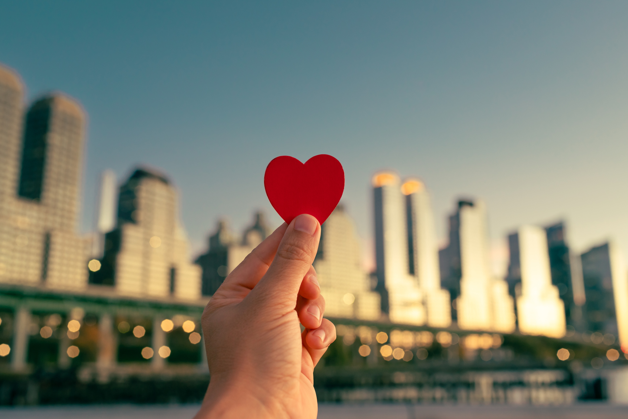 A wooden heart being held up against a city skyline.