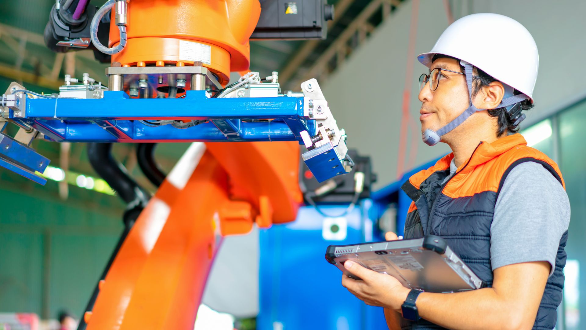 A robotics engineer inspects a palletizing robot by computer tablet on a work site.