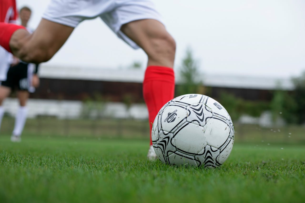 A man's legs in football boots and shorts, kicking a football. 