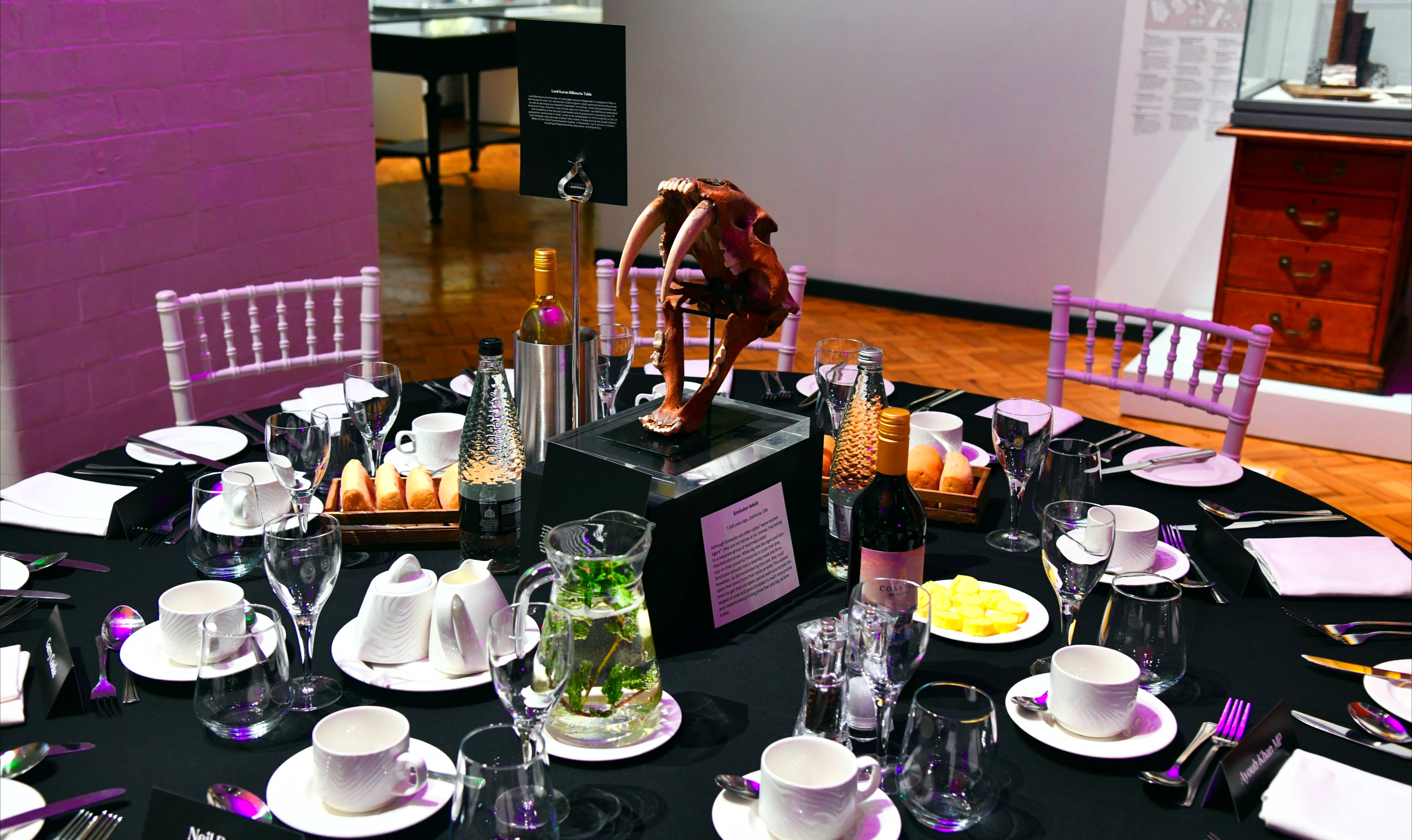 A Smilodon skull stands at the centre of a formal dinner table.