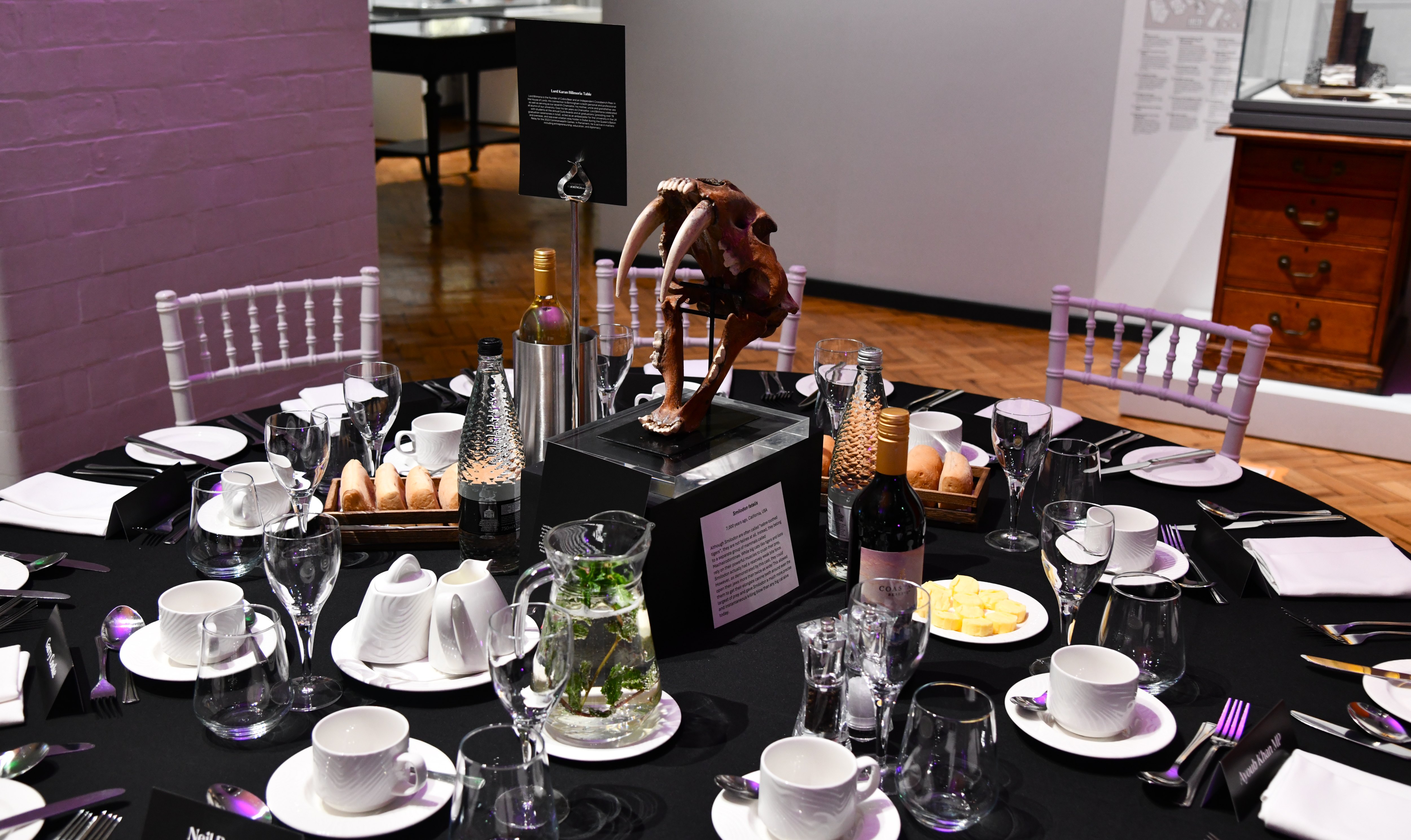 A Smilodon skull stands at the centre of a formal dinner table.