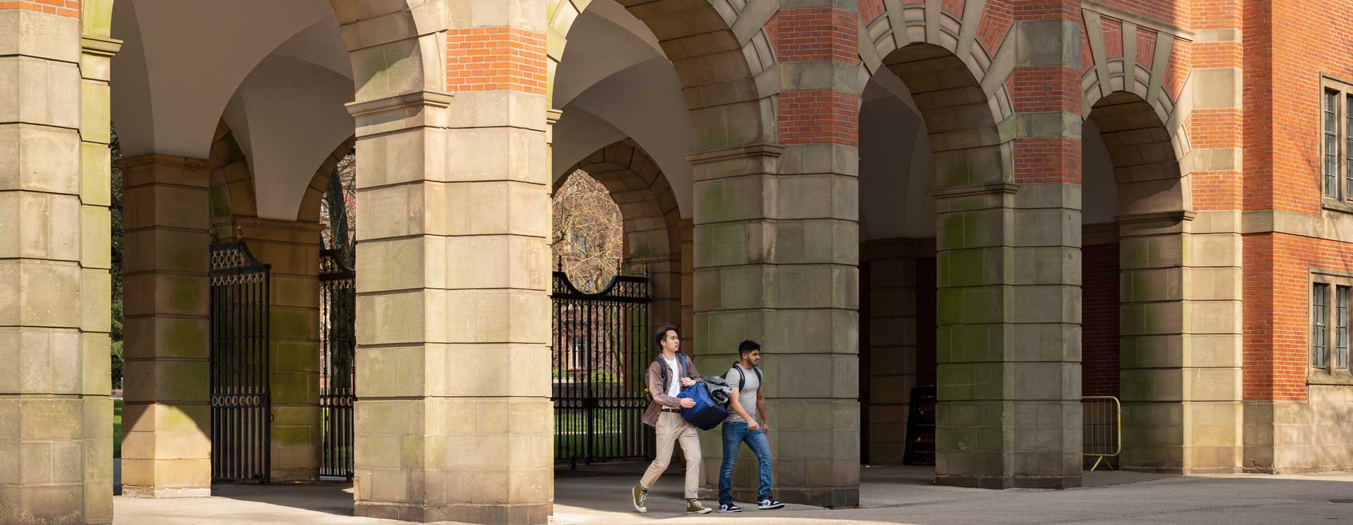 student walking under the Law School arches at the University of Birmingham on a sunny day