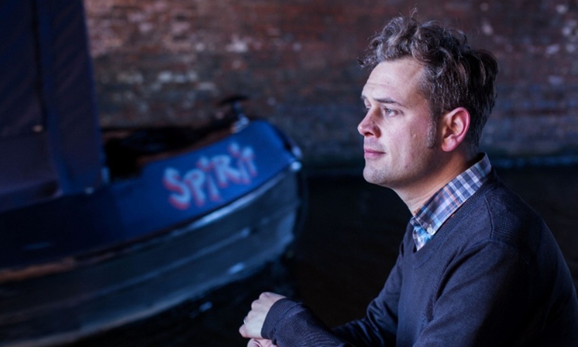 Luke Kennard sitting beside a moored boat with the word 'Spirit' painted on it.