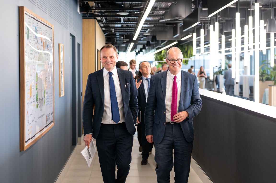 Two men wearing suits and ties walking down a corridor