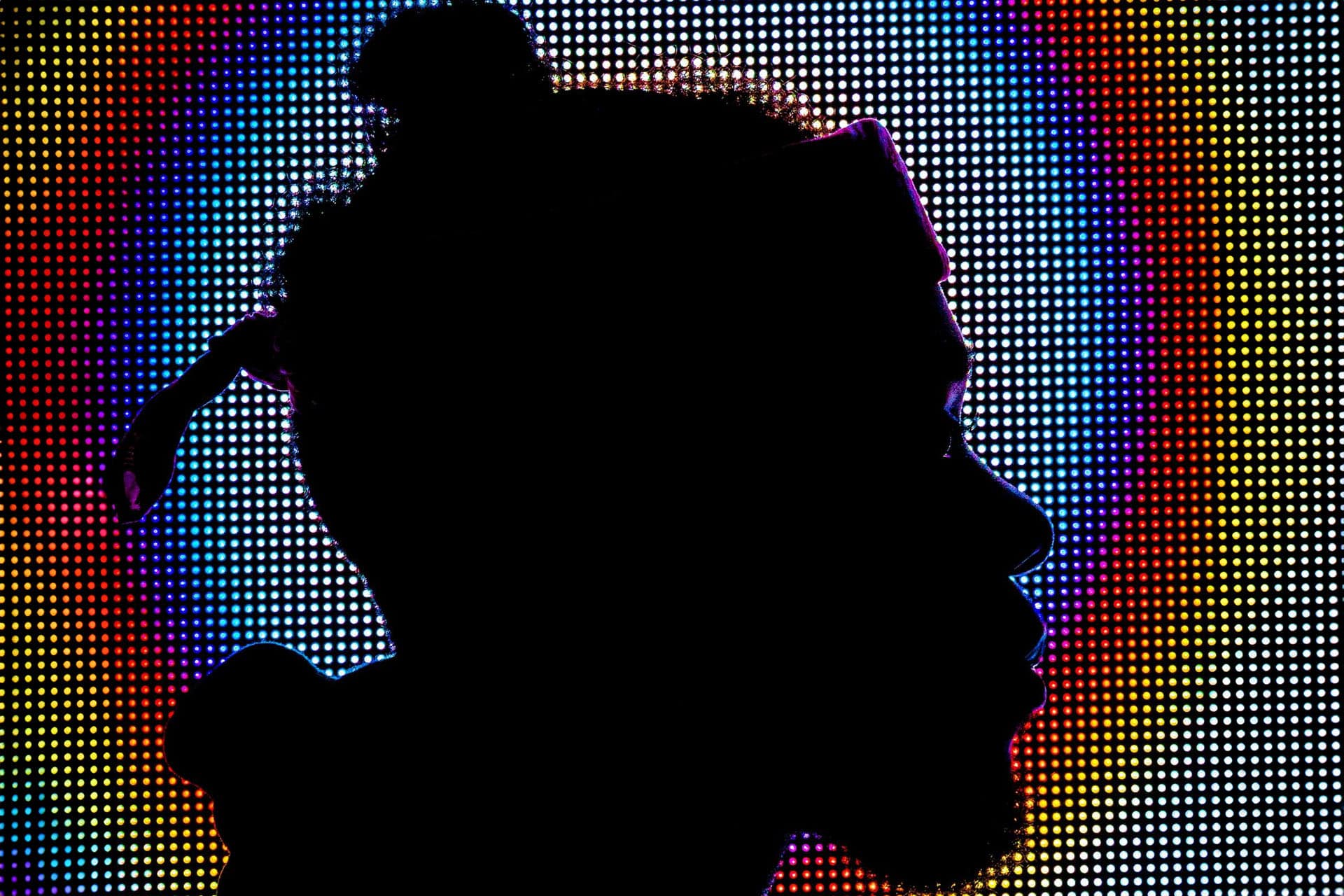 Silhouette of man's head against a multicoloured dot matrix neon background.