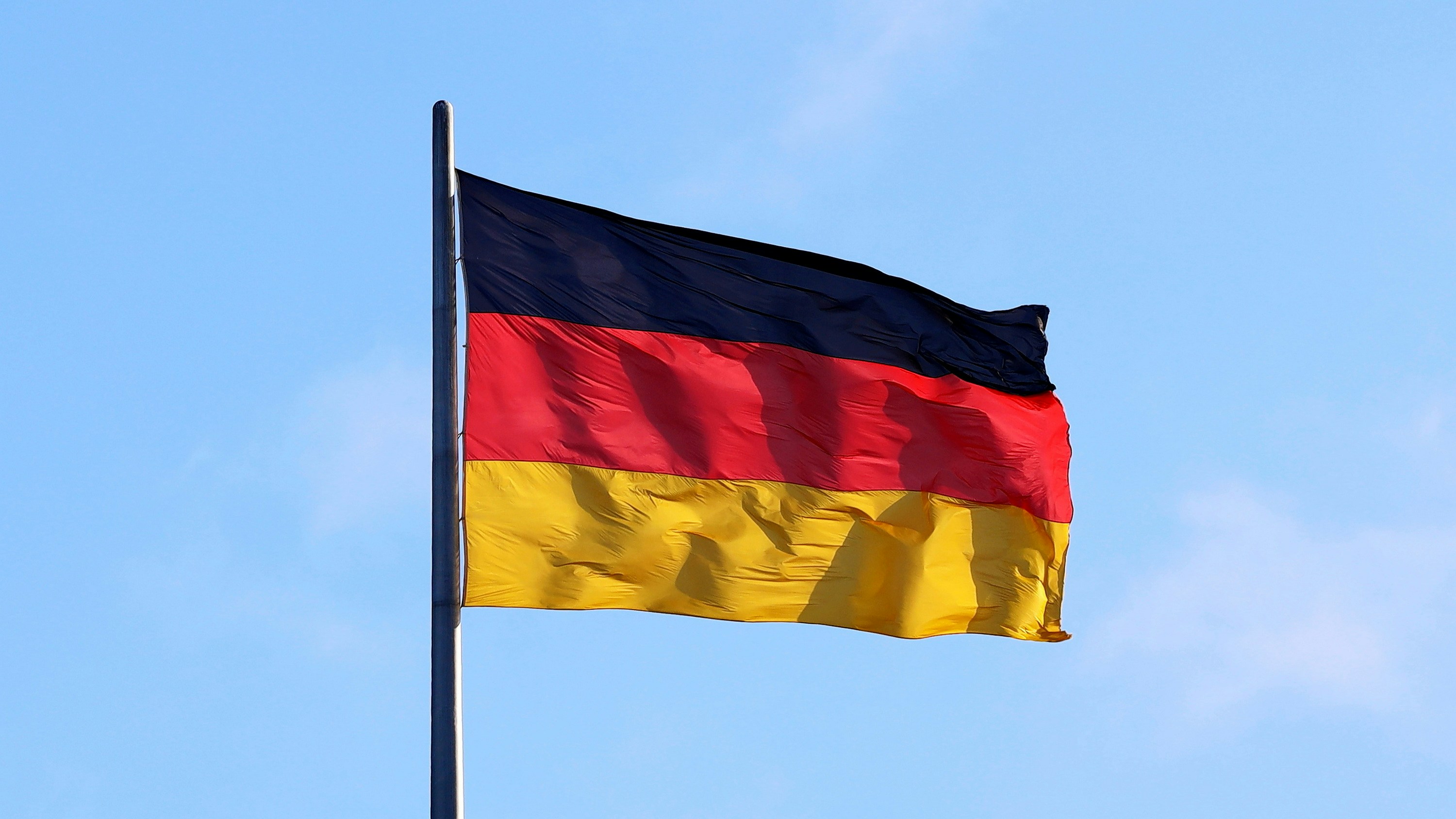 The German flag flies against a blue sky