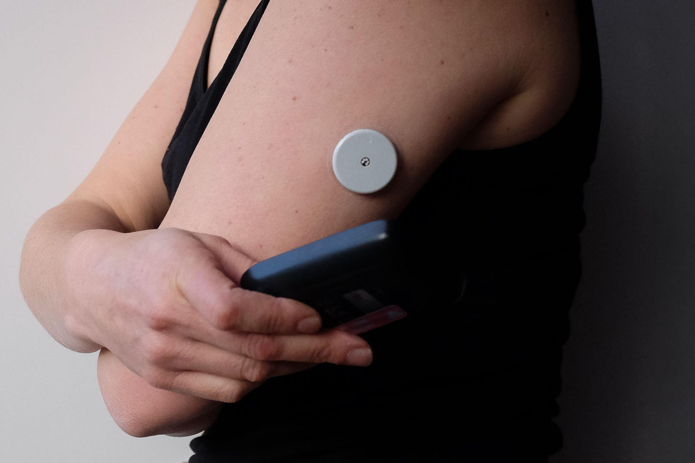 A woman holding a smartphone near a small, circular medical device on her left arm