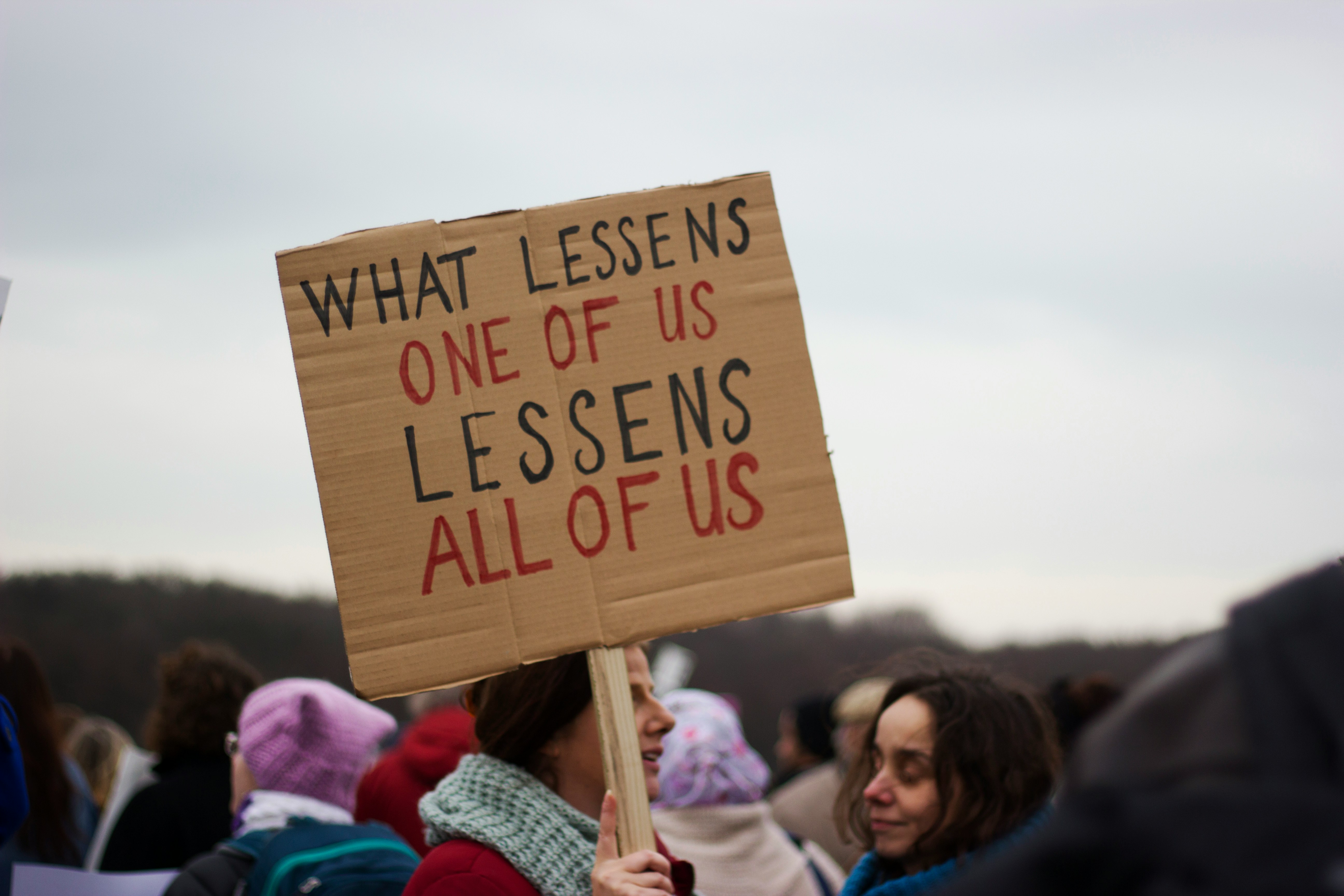 Women protesting with one holding a sign saying: 'What lessens one of us lessens all of us'.