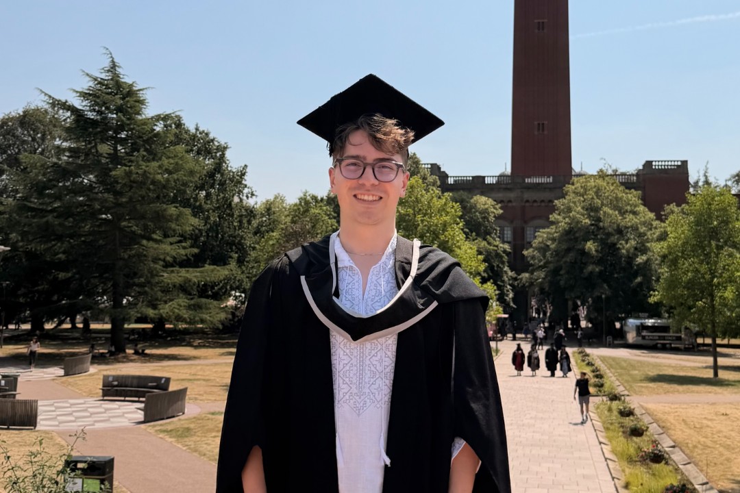 Man in graduation robes and cap stands in front of Old Joe