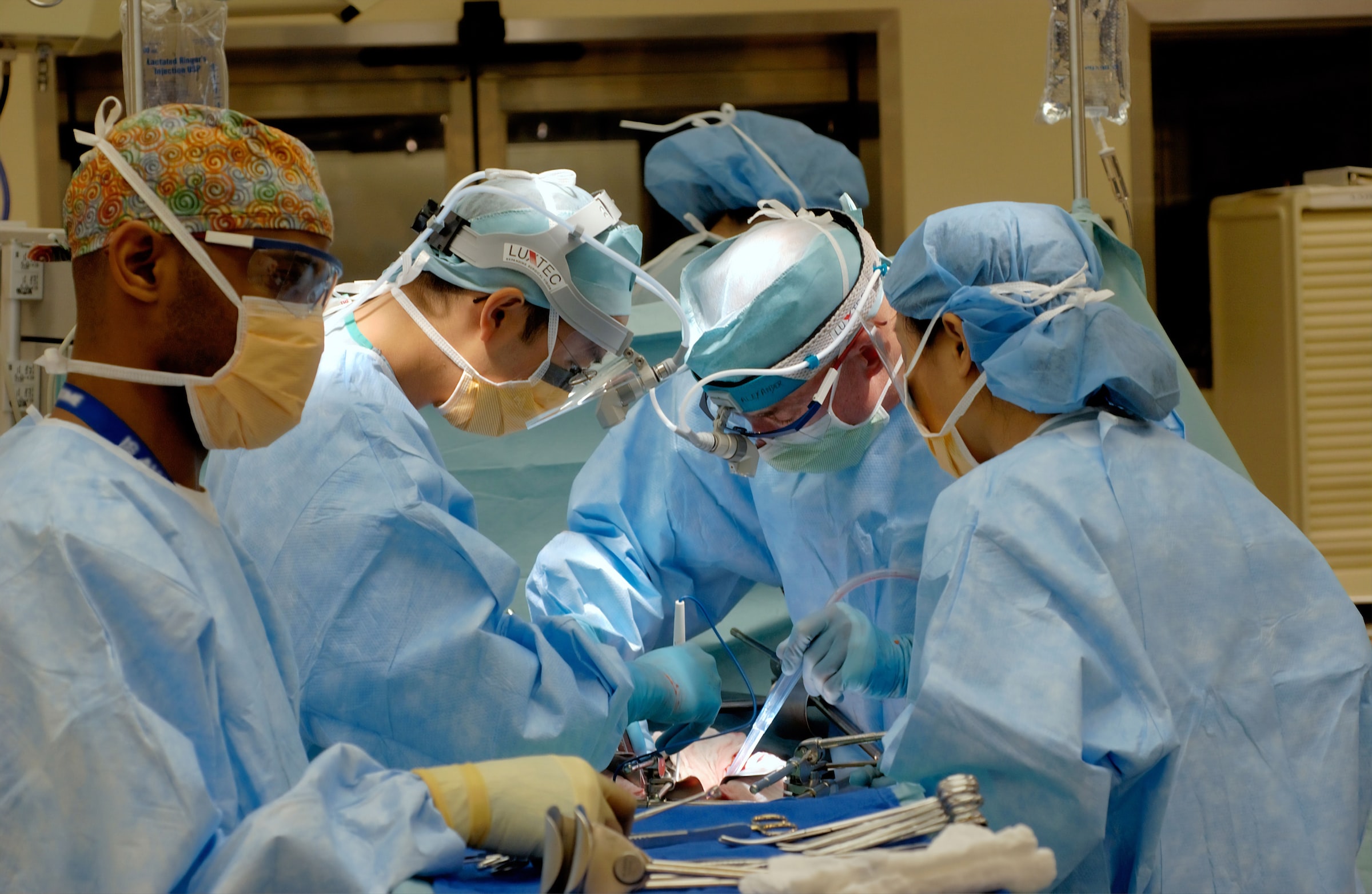A team of surgeons in operating theatre wearing blue gowns, skull caps and face masks