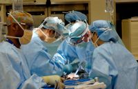 A team of five surgeons during an operation in an operating theatre, wearing blue gowns, gloves and PPE