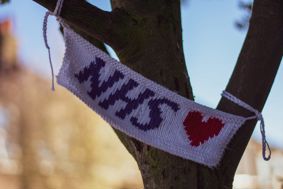 An NHS at 75 knitted banner wrapped around a tree