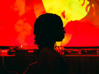 A stylised image of NikNak in front of a turntable with a red and yellow image behind her, casting a red glow to the image