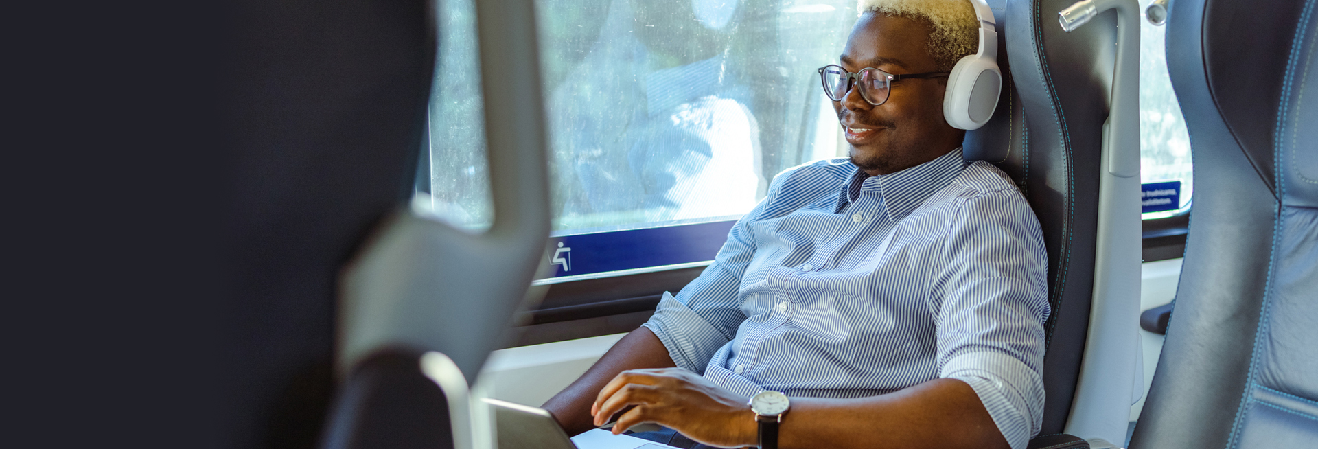 Student on the train with headphones on and working on their laptop