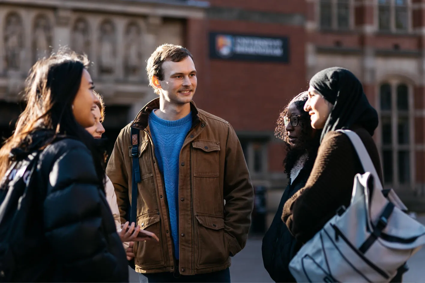 Five students standing in front of the Aston Webb building chatting and smiling