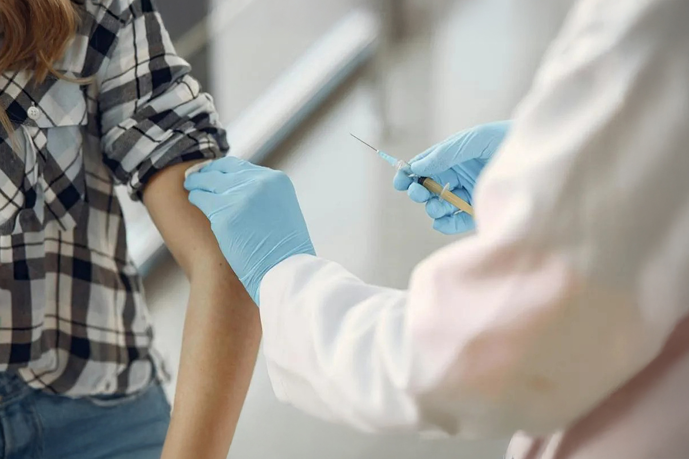 A doctor wearing blue Latex gloves vaccinating a young woman