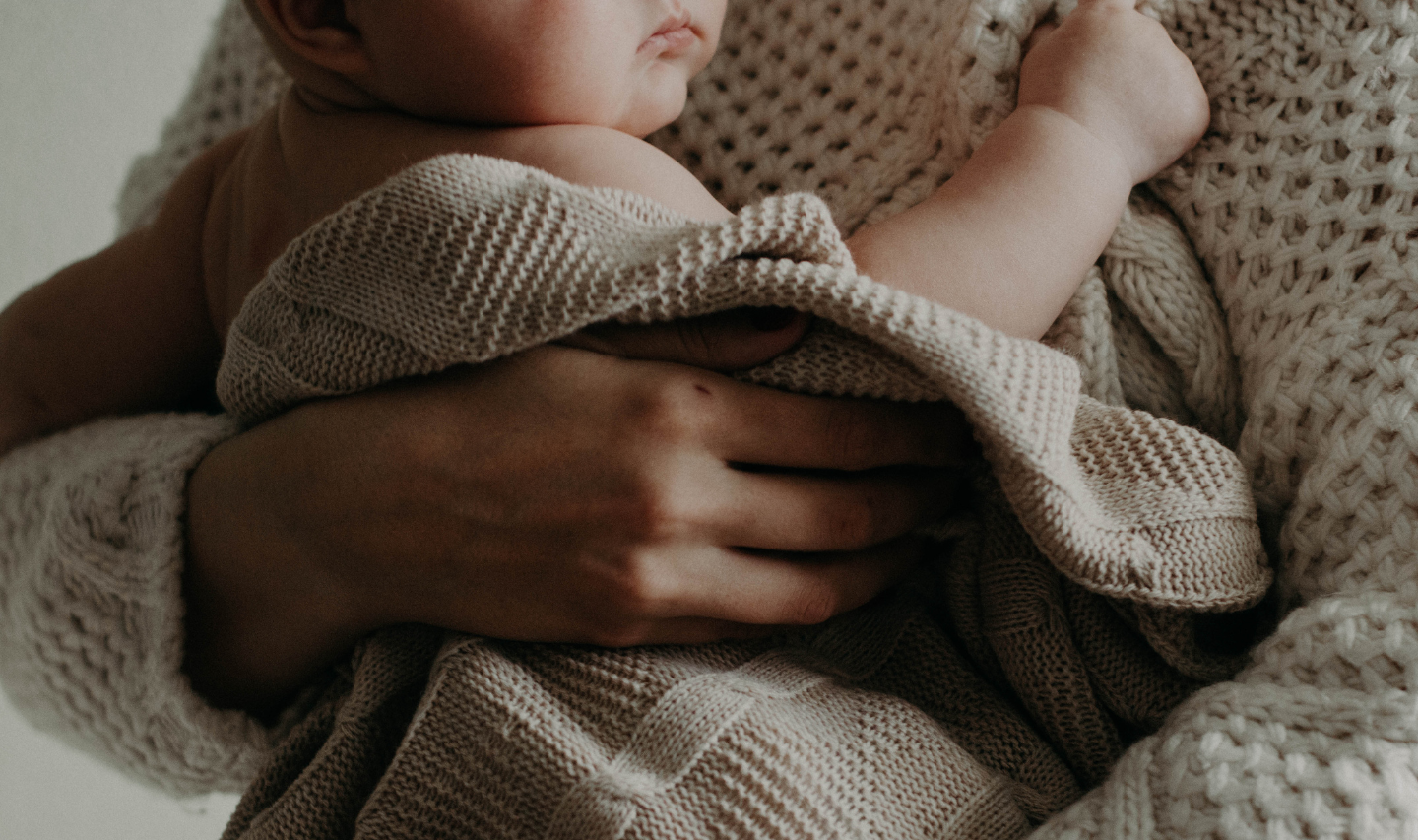 a close up image of mother wearing a cream knit jumper and holding a baby