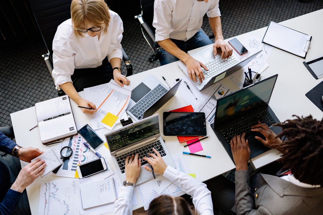 People working at a table on laptops and with paper together.