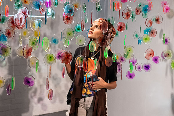 Woman looking at lots of petri dishes hanging up in all different colours
