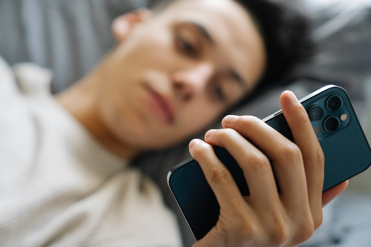 A teenage boy is lying on his bed and looking at his smartphone.