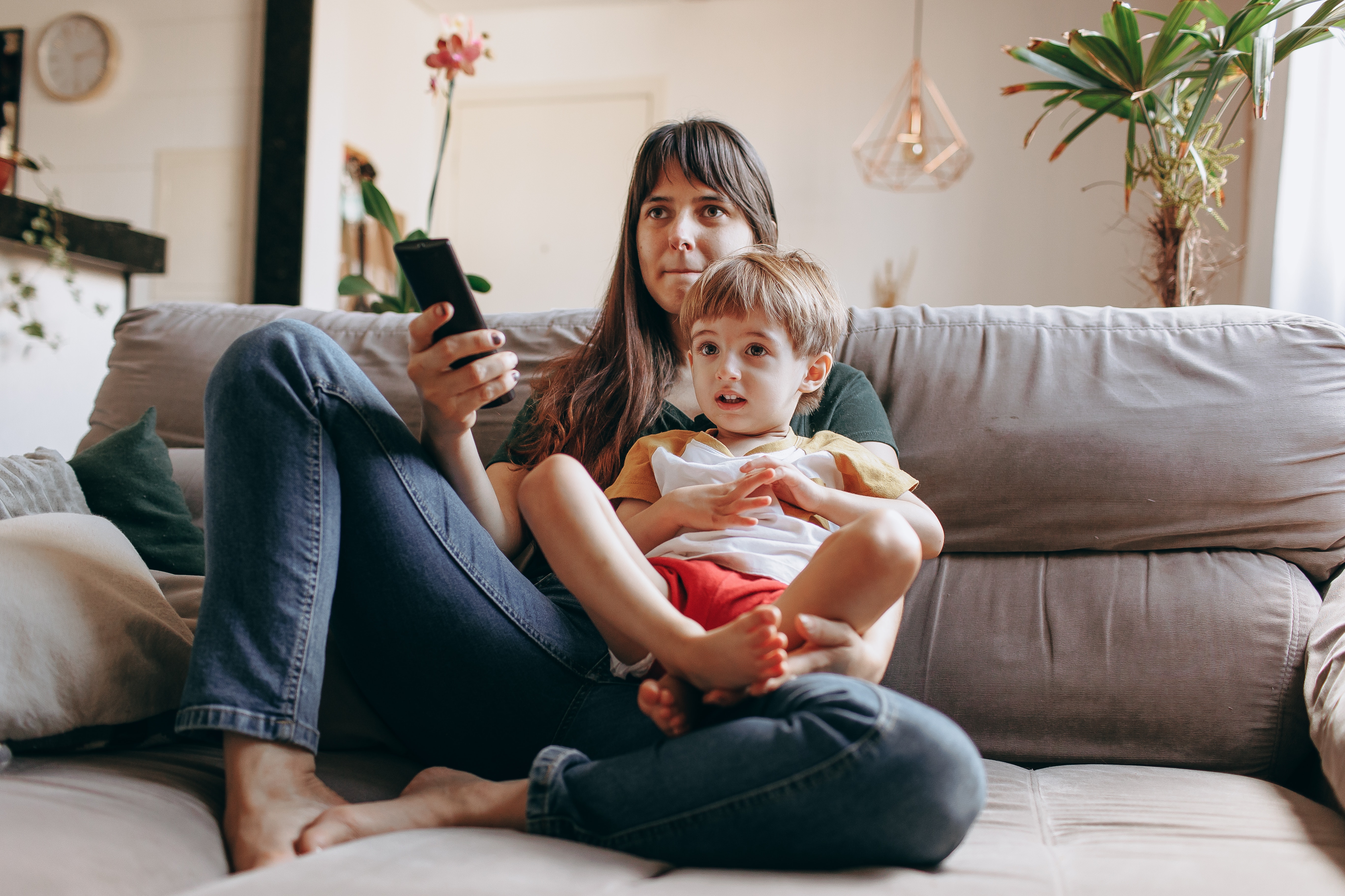 Young son and mother watching TV together while sitting on couch