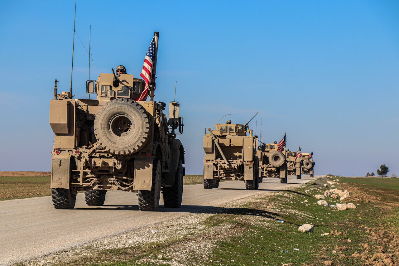 US army vehicles driving down a road with US flags.