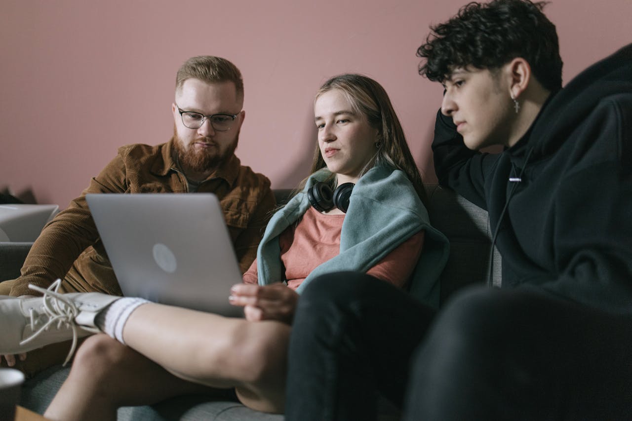 A man, sitting on a sofa with a young woman and a man with a laptop, offering guidance. 