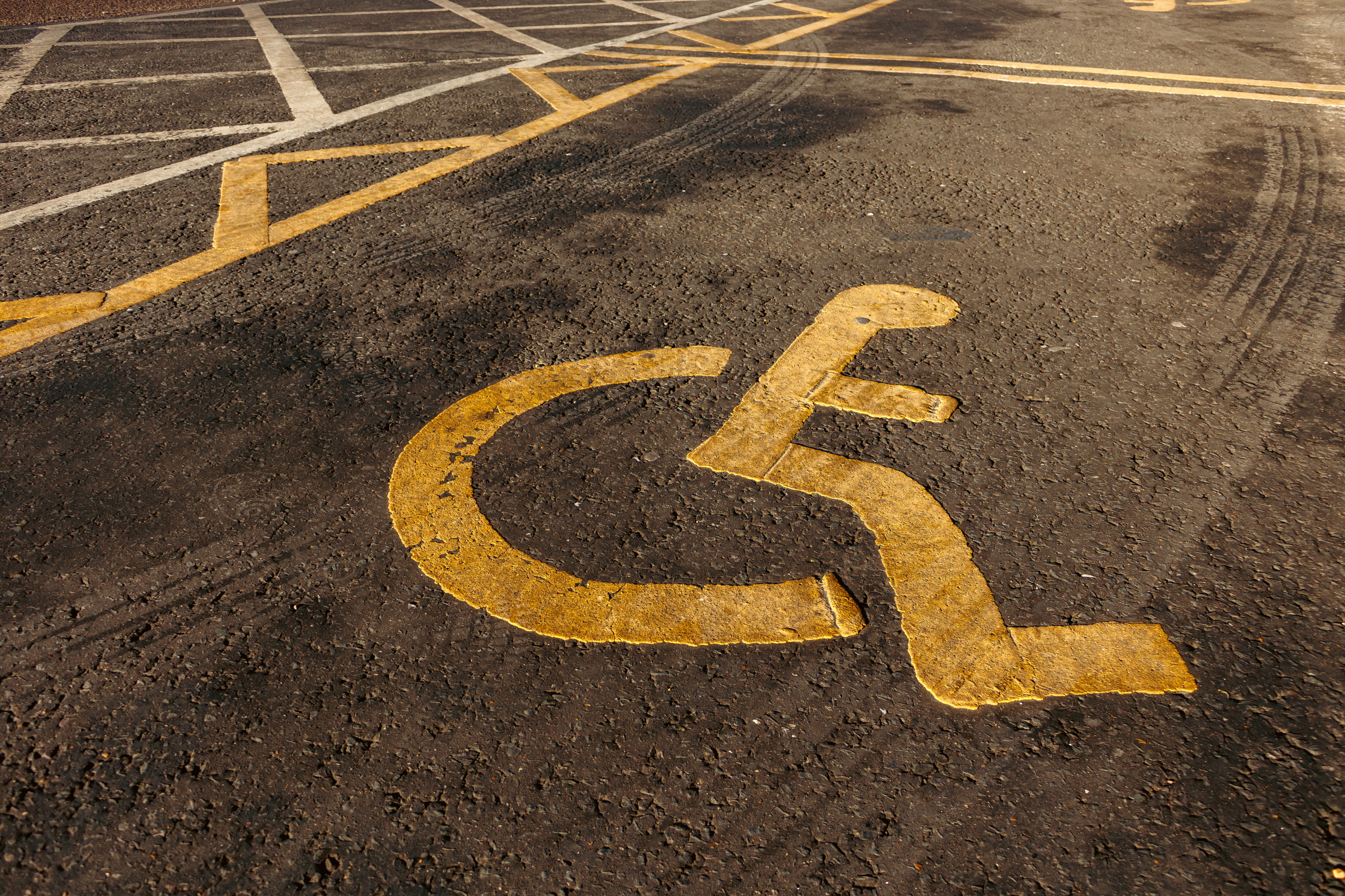 Disability symbol of figure in wheelchair printed in orange paint on a black car parking space