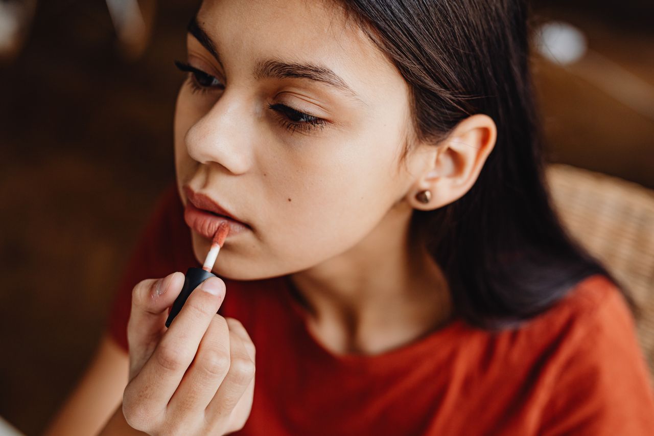 A young girl putting on liquid lipstick