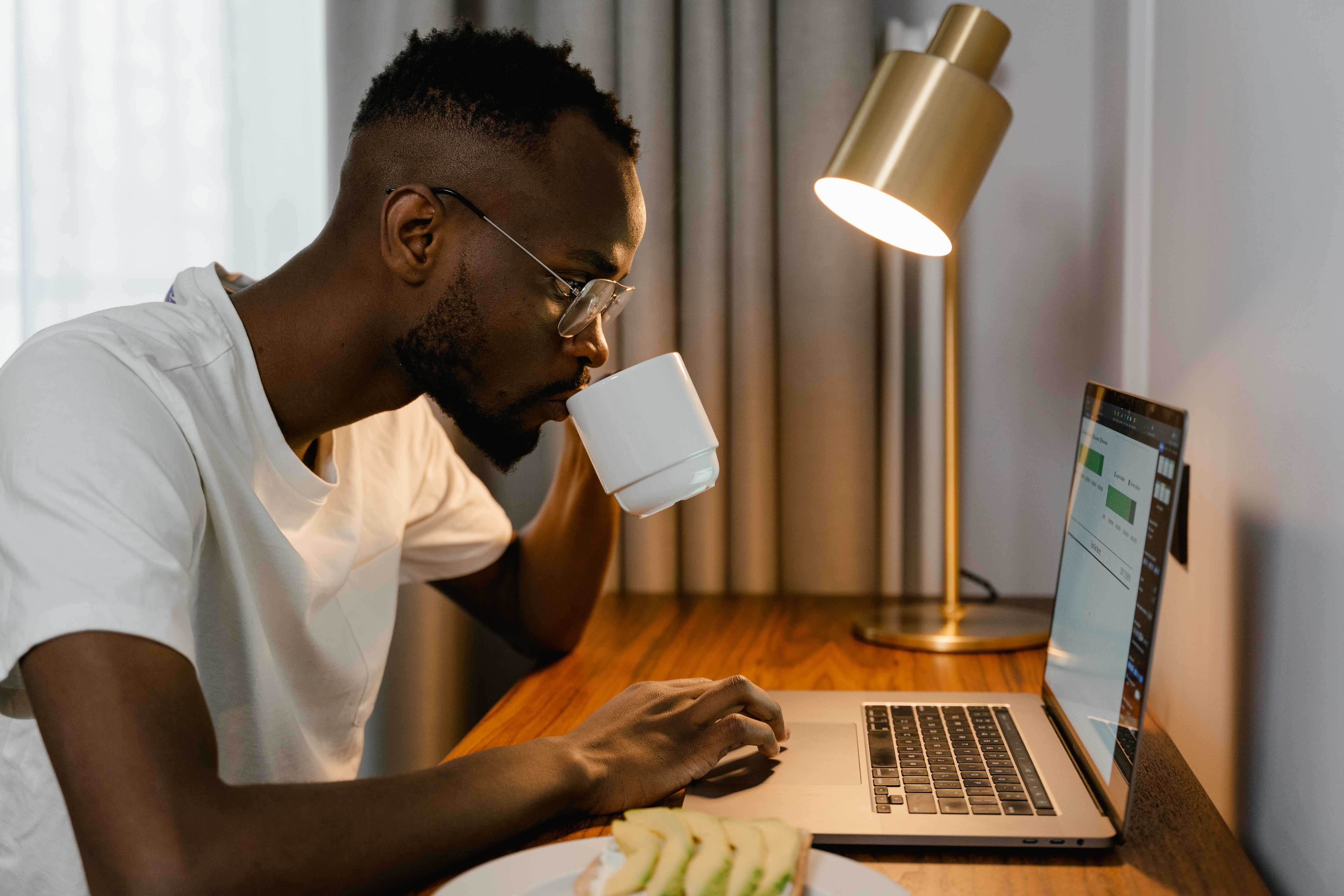 Man sipping from a coffee mug while working on a laptop at home