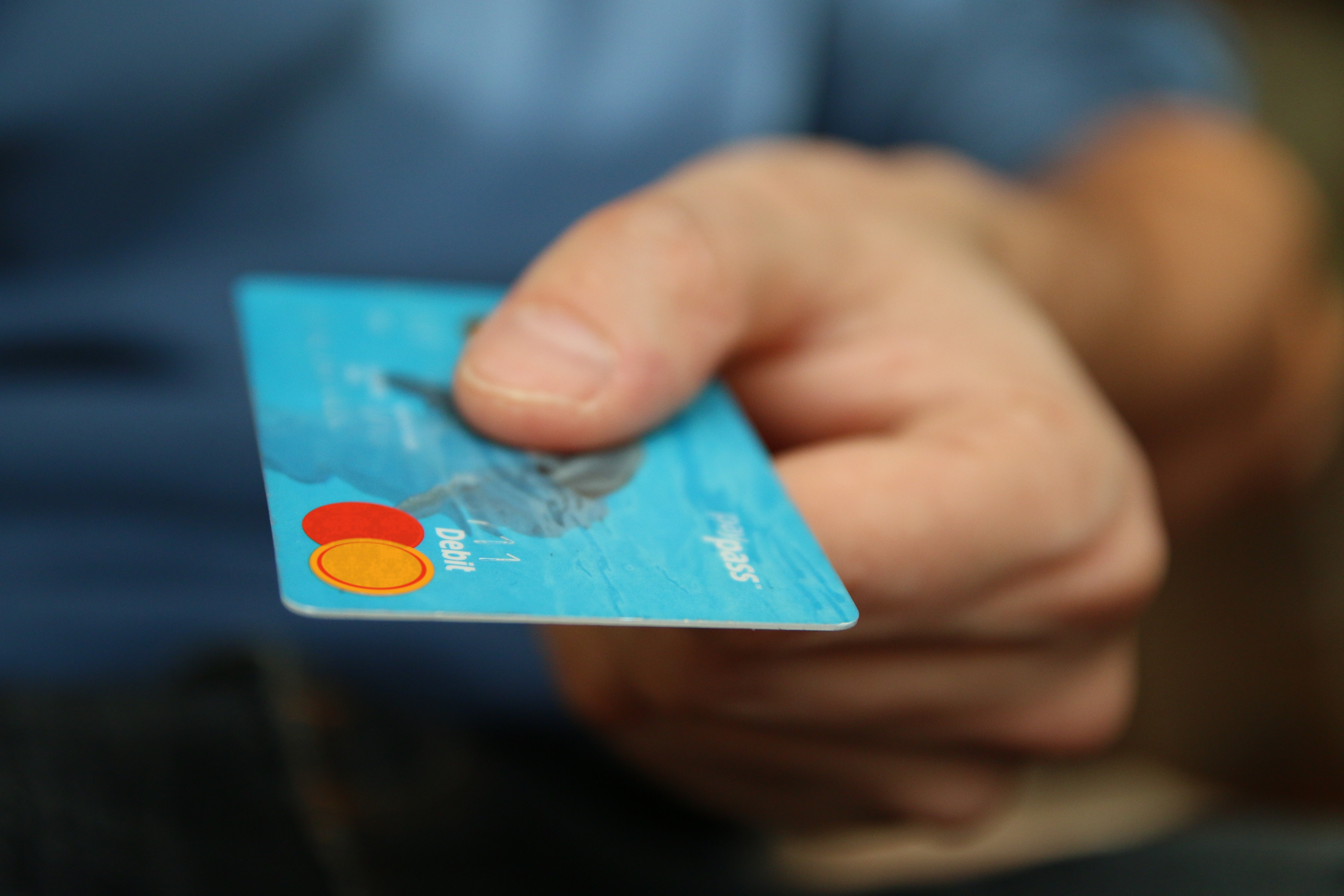Close up of a hand proffering a debit card towards the viewer