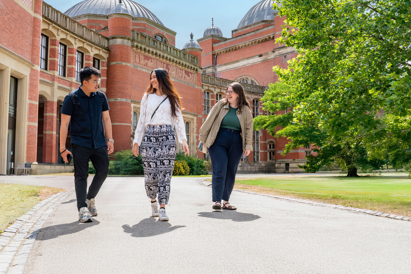 Three smiling students walking in Chancellor's Court with the Aston Webb building in the background