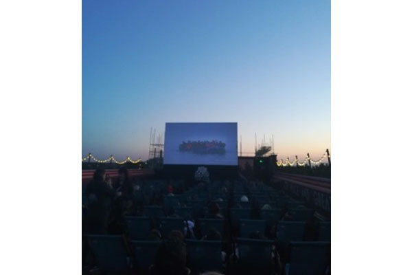 An audience watching a presentation on a large screen outside