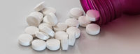 Round white pills spilling out onto a white surface out of a pink pill bottle