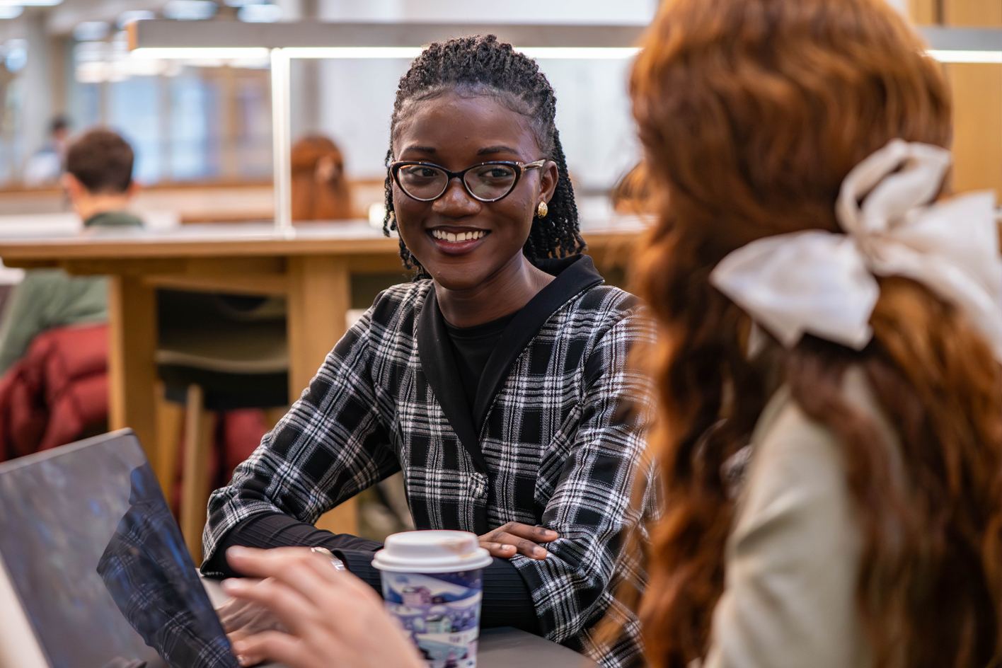 A smiling female student chatting to a friend with an open laptop in front of them