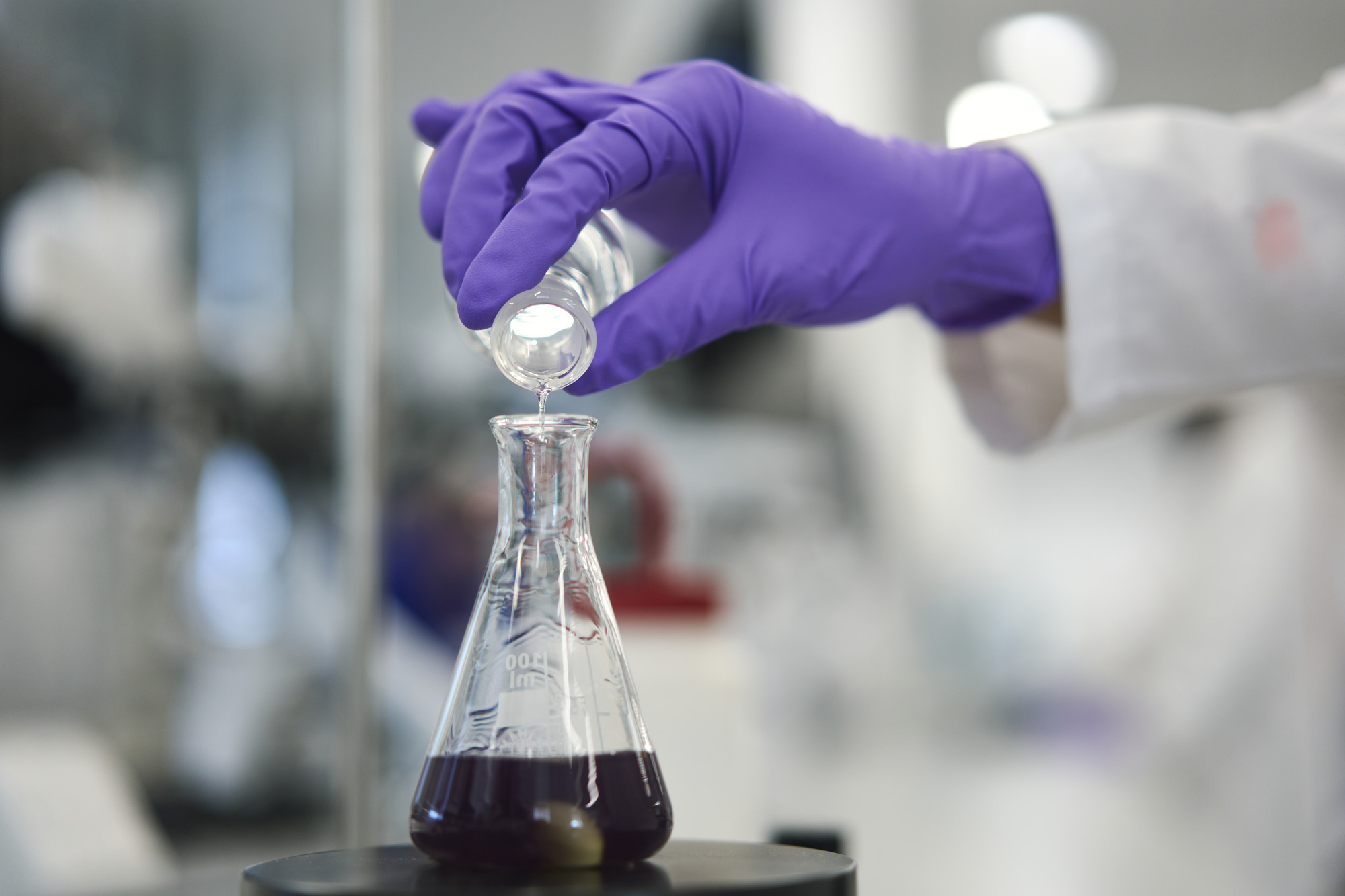 Person in lab coat pours liquid into a conical flask