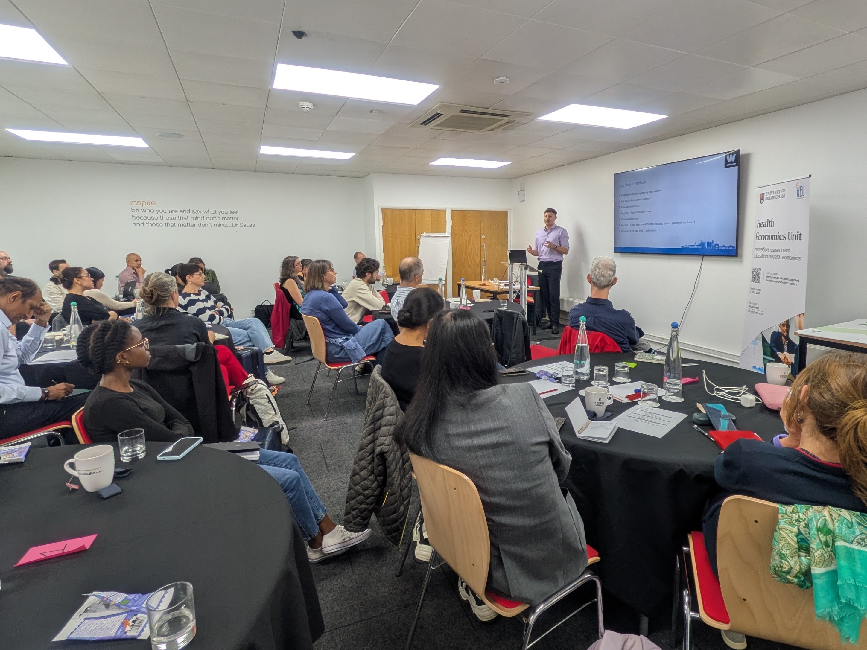 A workshop with a large room full of people listening to a man speak at the front of a room.