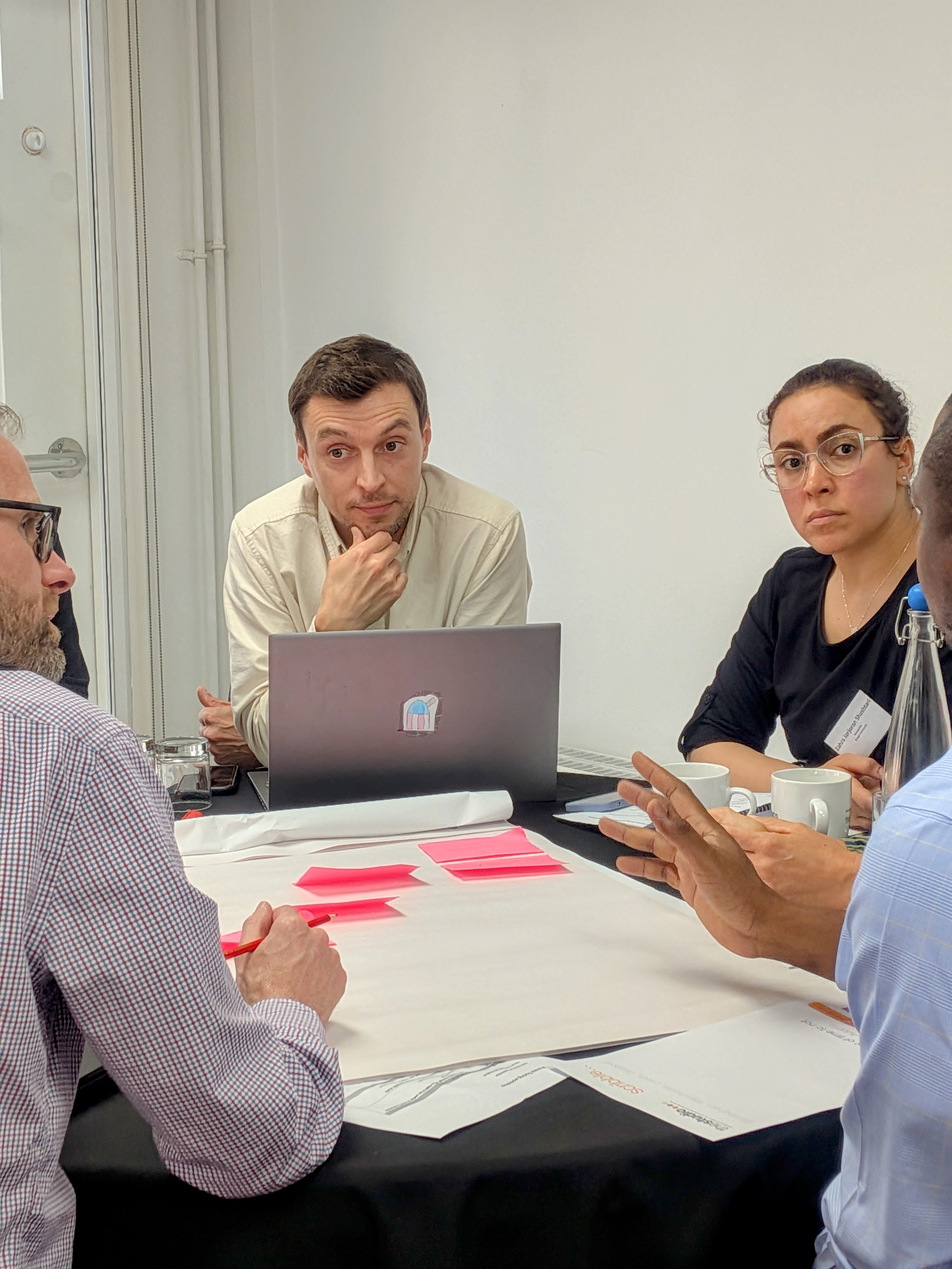 Four people (two men and two women) in discussion during a workshop exercise with pink paper in front of them.