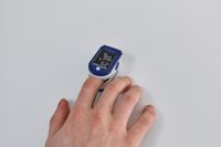 A pulse oximeter used to measure blood flow and blood oxygen levels clipped to an adult's hand