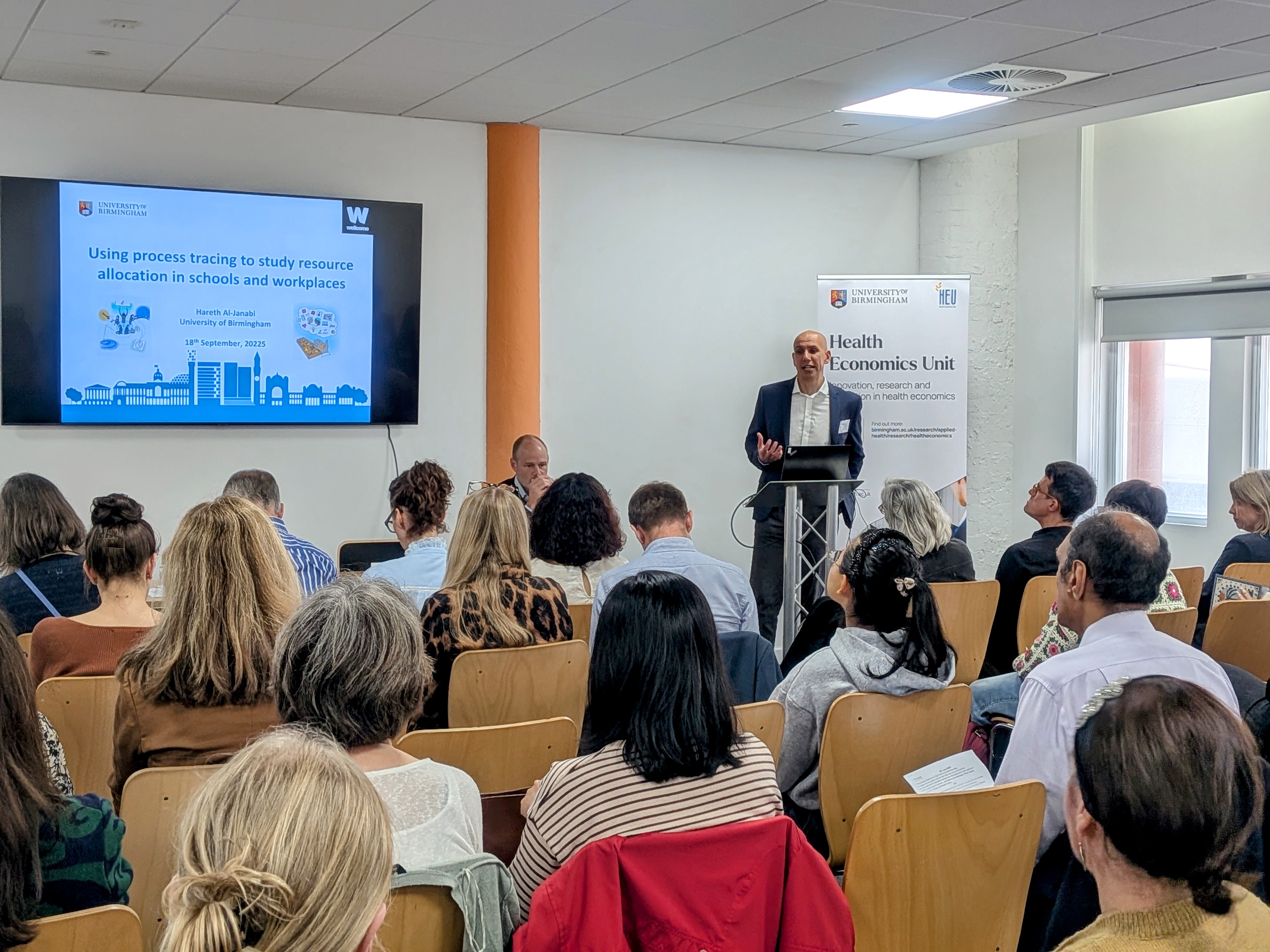Professor Hareth Al-Janabi presenting a session to an audience with a PowerPoint slide titled 'Using process tracing to study resource allocation in schools and workplaces'.