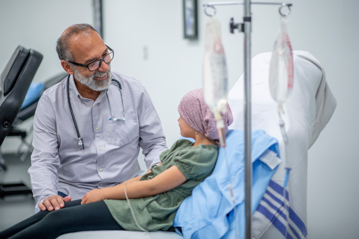 A smiling doctor in consultation with a young girl hooked up to a drip, wearing a head scarf