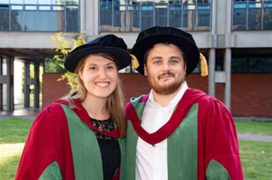 Sam and Amanda Cruchley in their Birmingham PhD graduation robes smiling at the camera.
